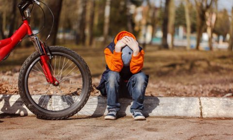 Photo of boy sitting on kerb with his head in his hands with a red mountain bike parked up next to him