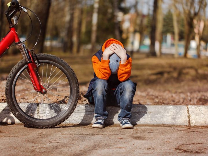 Photo of boy sitting on kerb with his head in his hands with a red mountain bike parked up next to him