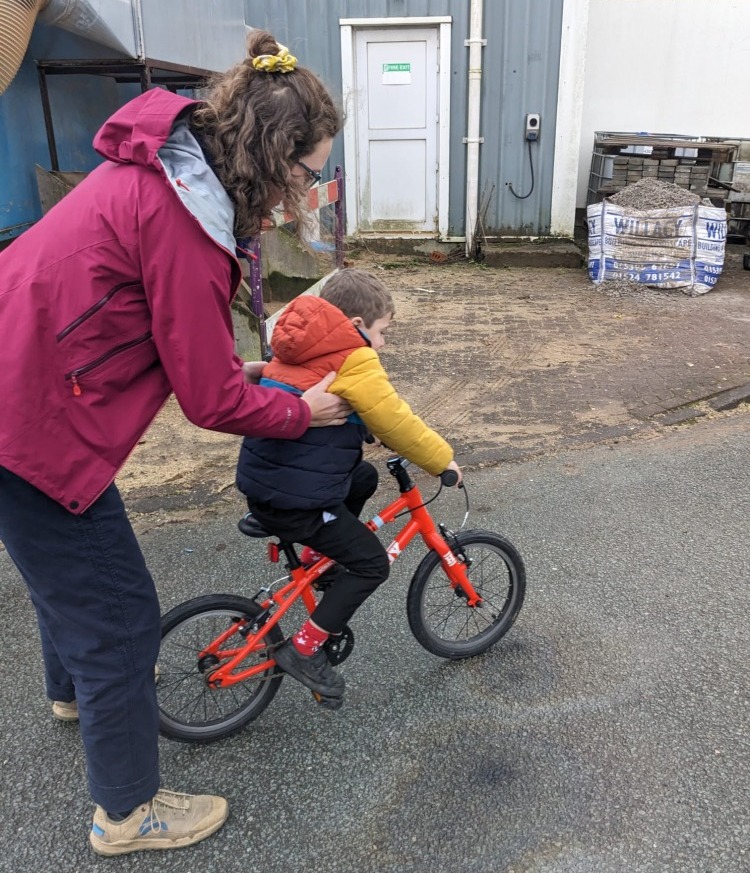 How to teach your child to ride a bike: adult holding child on first pedal bike to support them