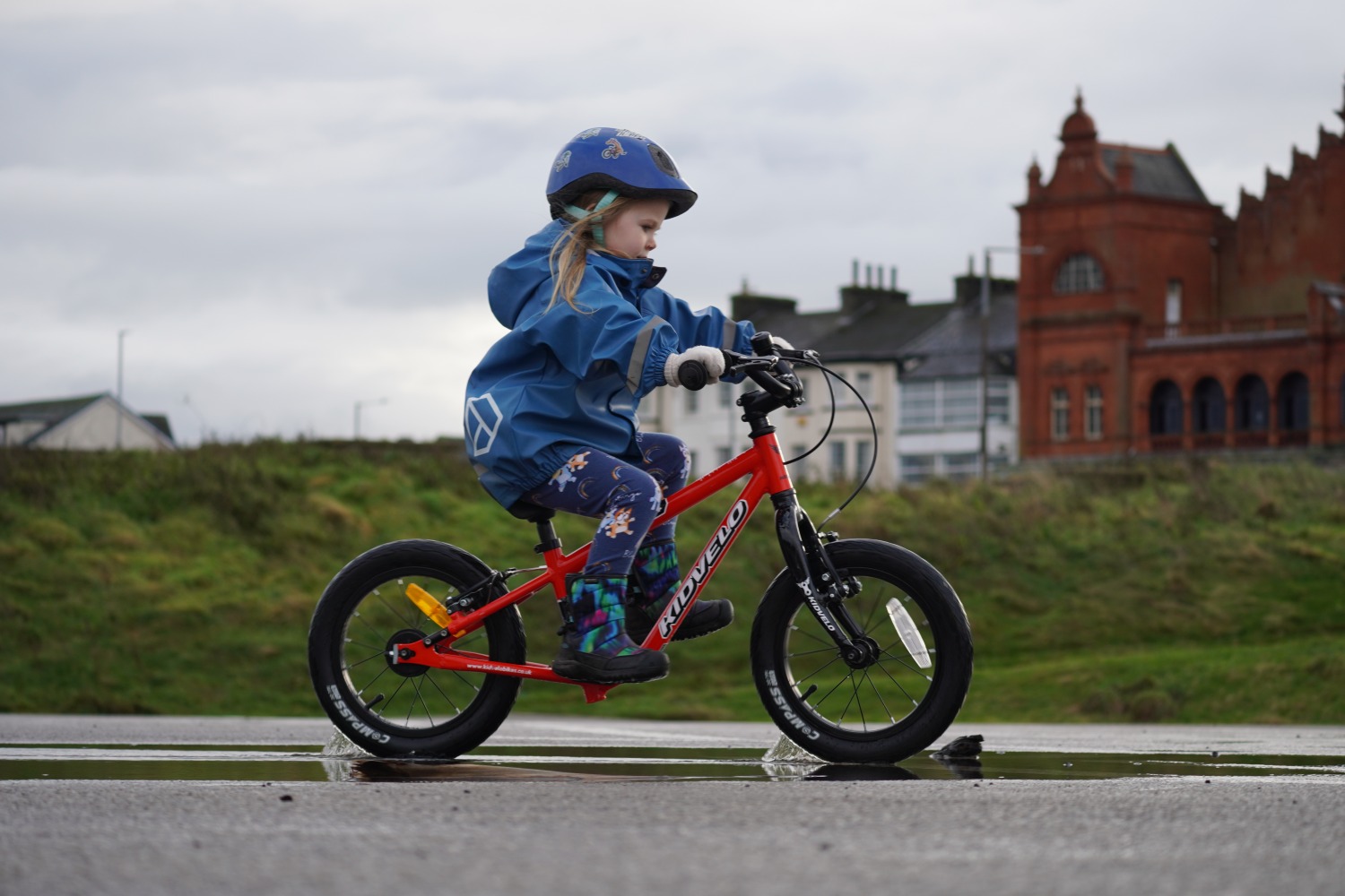 a girl in a blue coat happily gliding on her kidvelo rookie 14 balance bike by the seaside