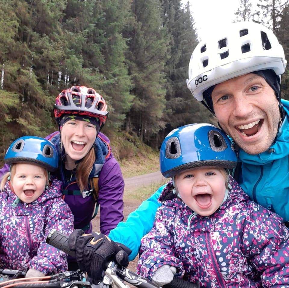 Cycling with babies and toddlers: Two parents and their twin daughters smiling at the camera in their bike helmets and waterproofs Two parents and their twin daughters smiling at the camera in their bike helmets and waterproofs