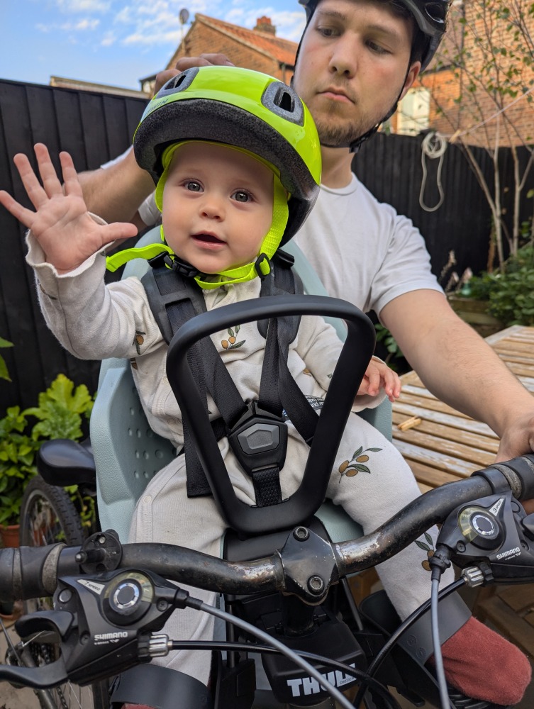 Thule Yepp 2 mini review:a little girl in a yellow helmet sat in a Thule Yepp 2 Mini front bike seat is waving at the camera