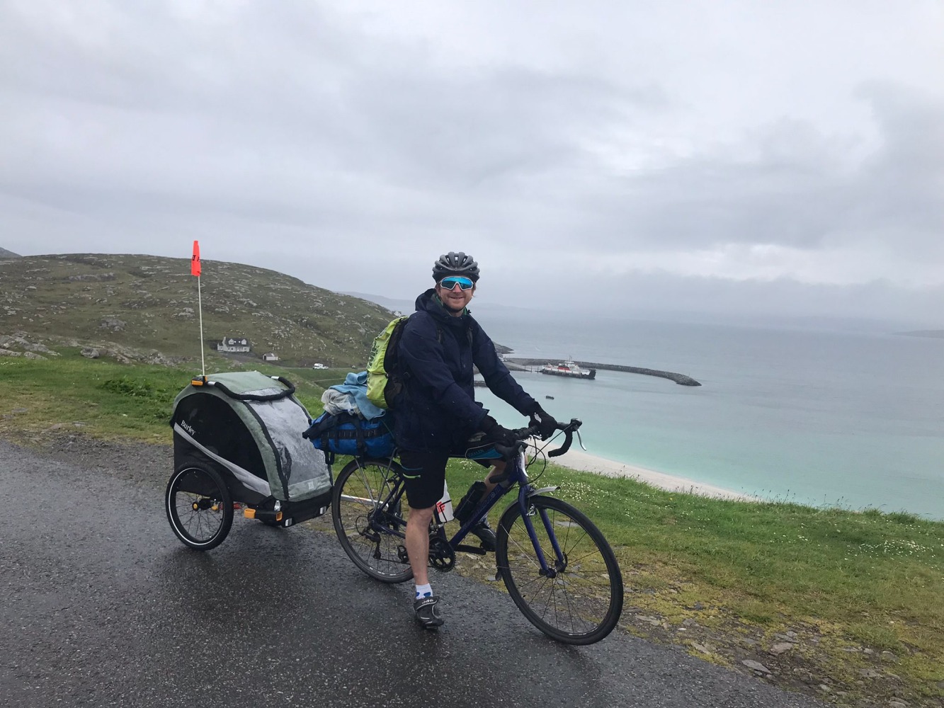 dad riding with the Burley D'Lite X child trailer in scotland with cliffs and the sea behind him