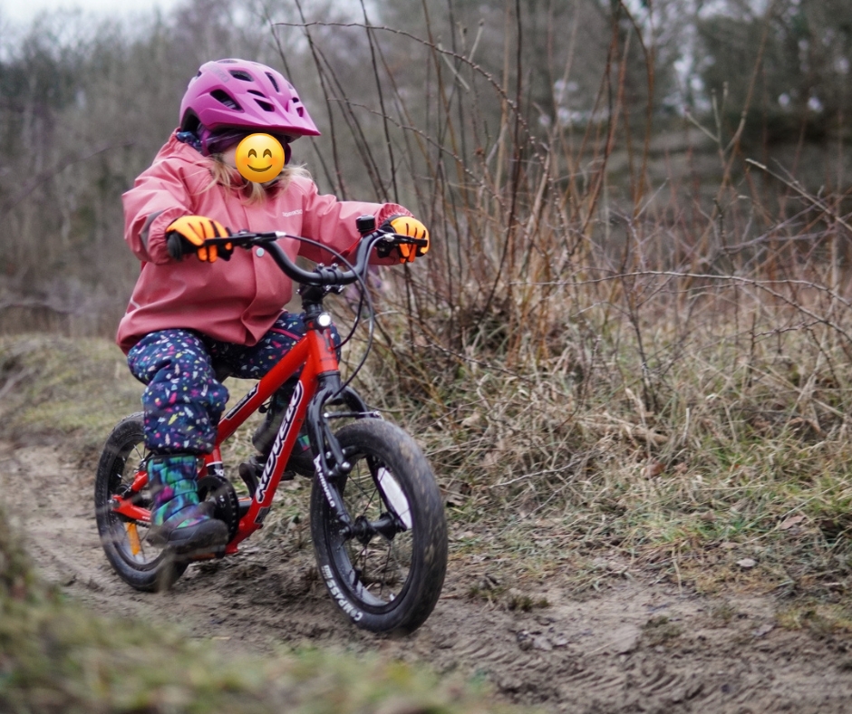 a girl in a pink coat happily gliding on her kidvelo rookie 14 balance bike by the seaside