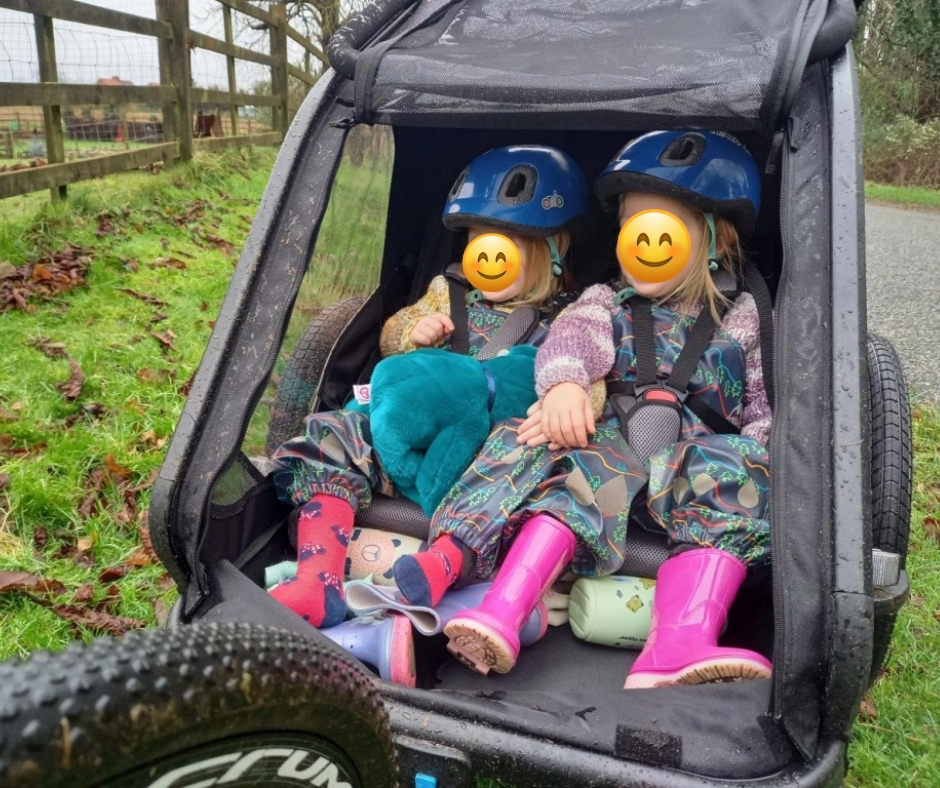 Two twin girls laughing and smiling in a bike trailer