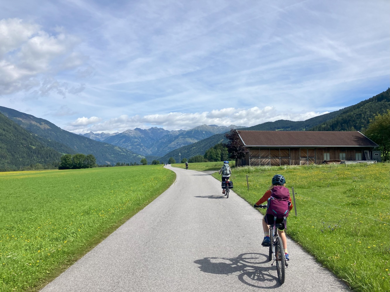 family cycling routes in Austria & italy: Bea's children cycling on a smooth path in a green field, seen from behind