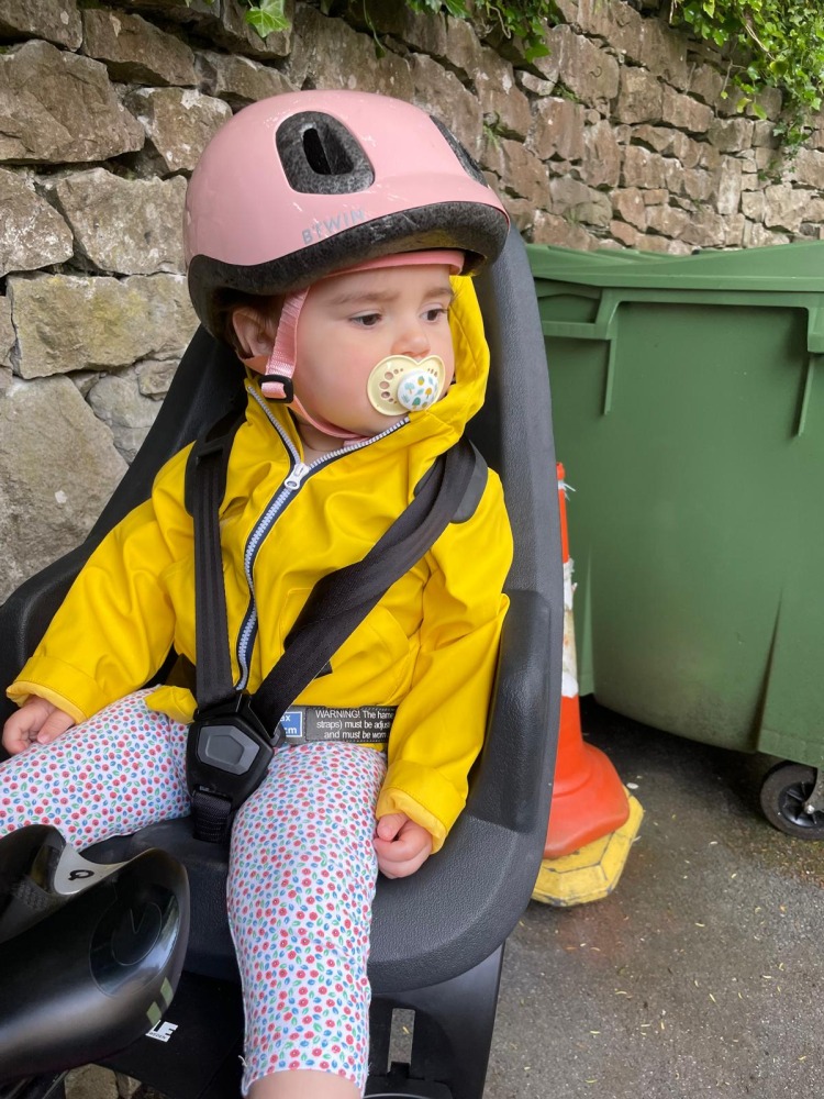 a toddler in a pink helmet and a yellow jacket on her rear bike seat