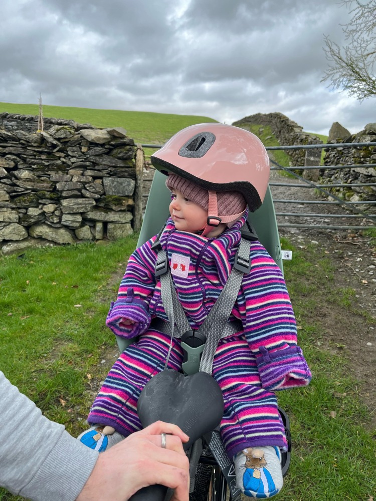 little girl in a stripy jacket with a pink btwin baby helmet on 