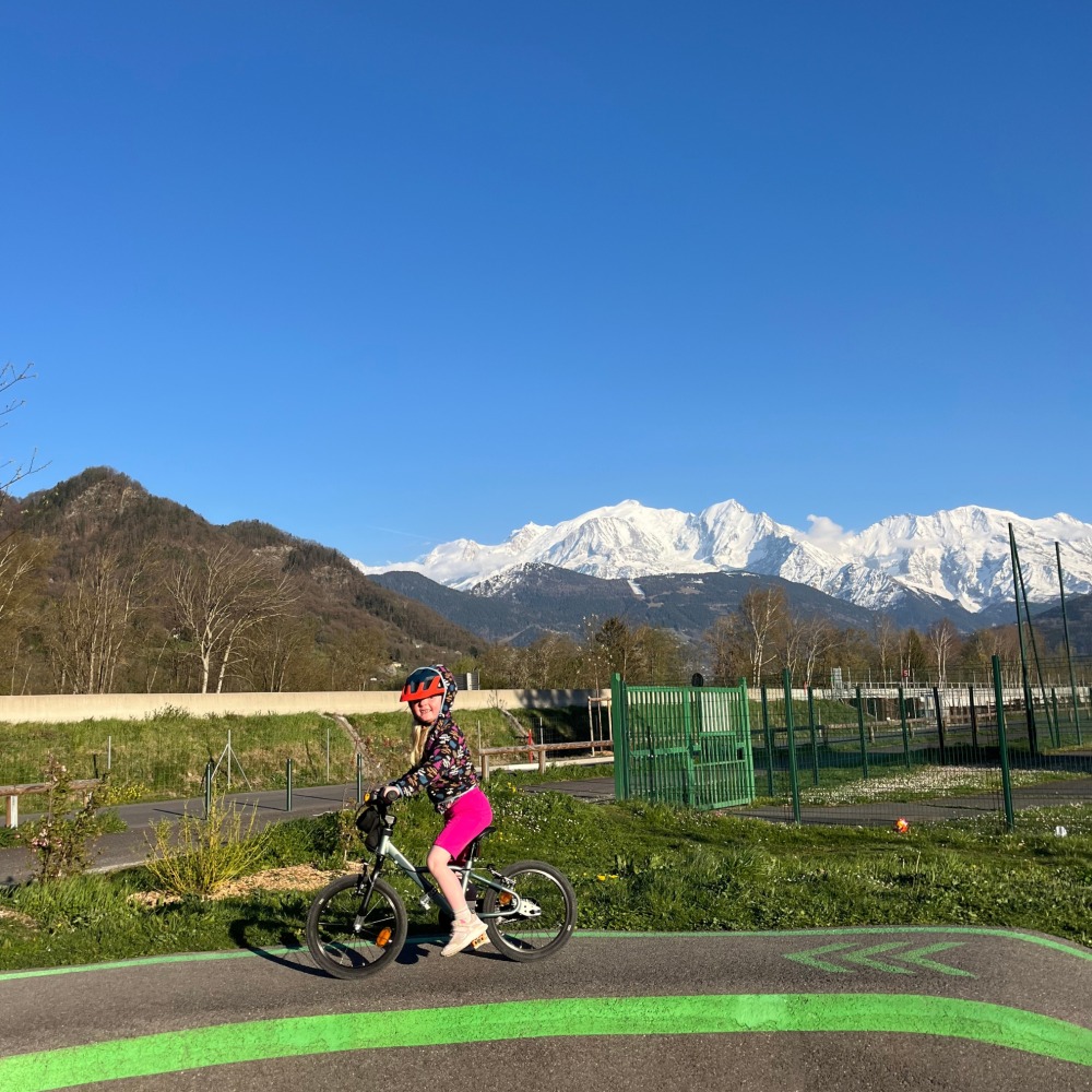 BTWIN 16 Discover 900 review- a girl in a flowry jumper and blue helmet riding on a pump trackwith a big snowy mountain behind her