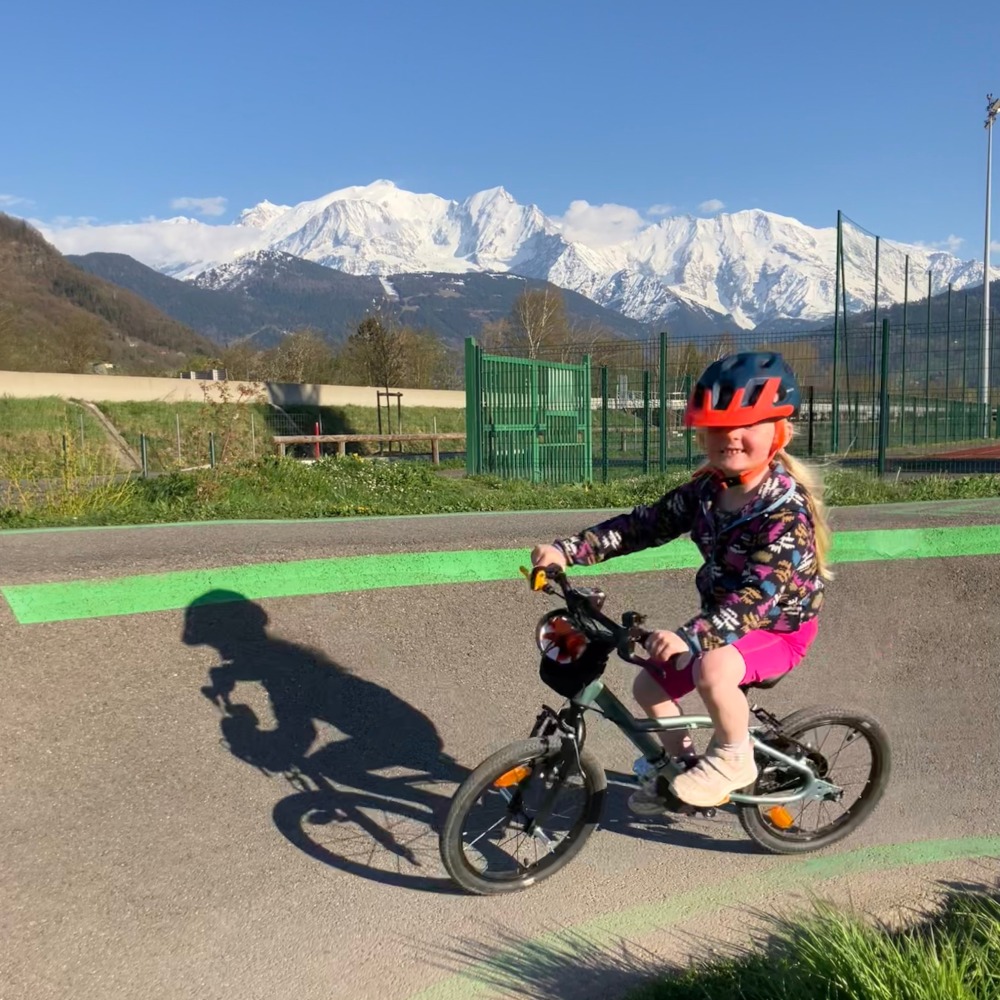 BTWIN 16 Discover 900 review- a girl in a flowry jumper and blue helmet riding on a pump trackwith a big snowy mountain behind her
