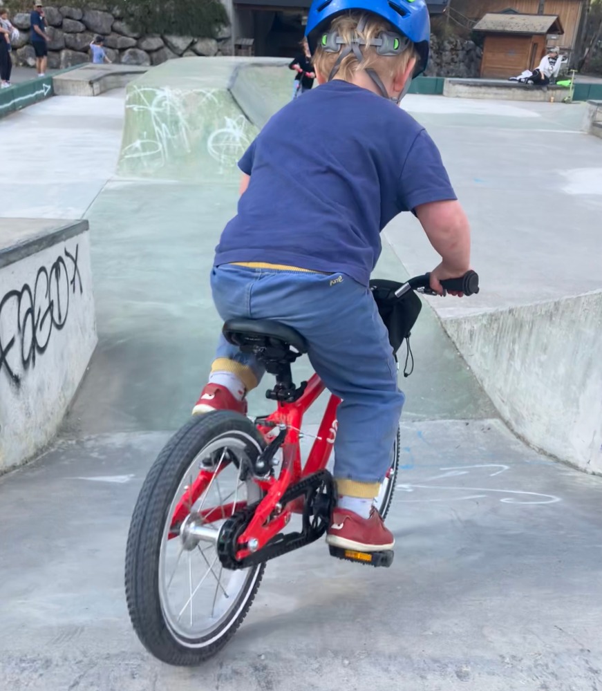 A little boy riding his red yomo bike with a blue helmet on a skate park