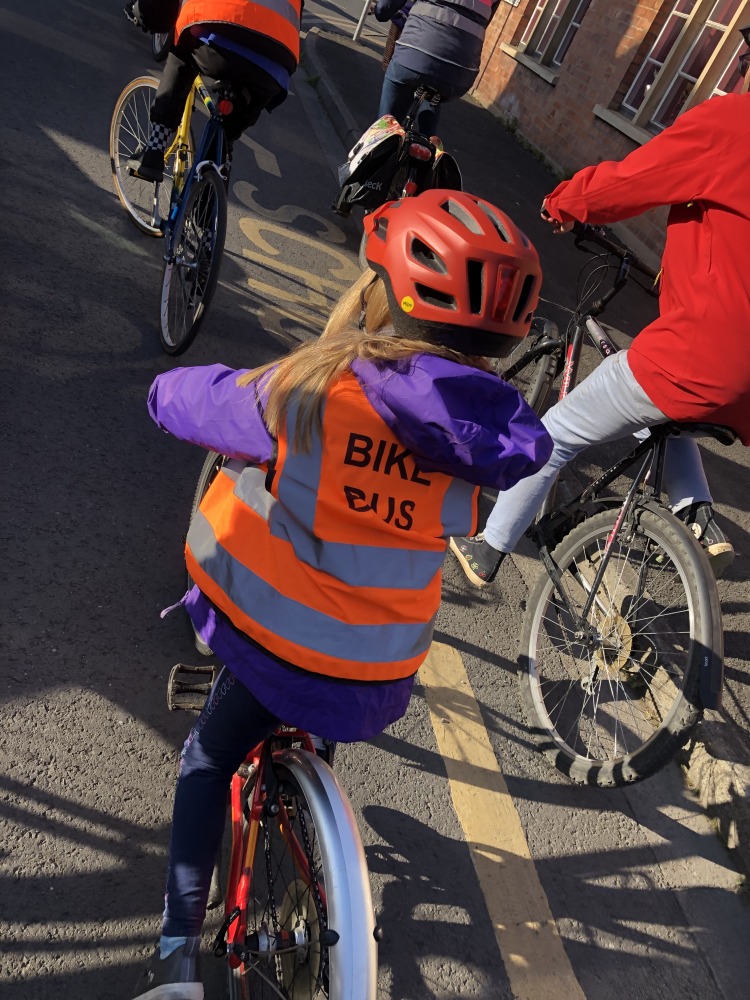 campaign for cycling infrastructure: Child riding a bicycle on a Bike Bus with a hi viz vest on saying Bike Bus