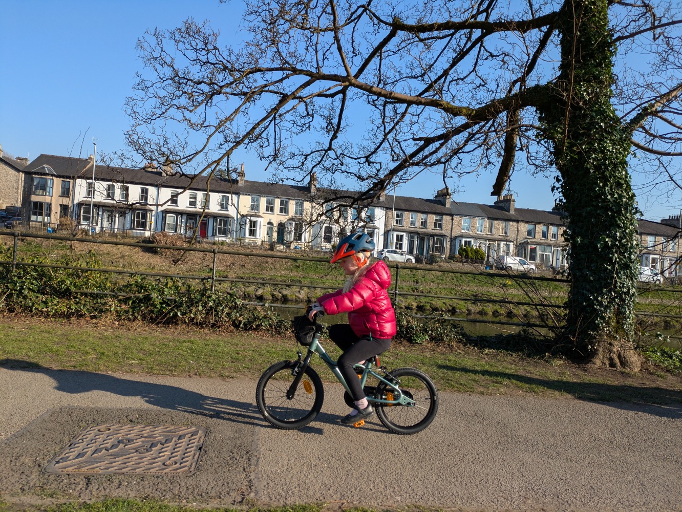 A girl in a pink jacket riding the BTWIN 16" discover bike by the river on a sunny day