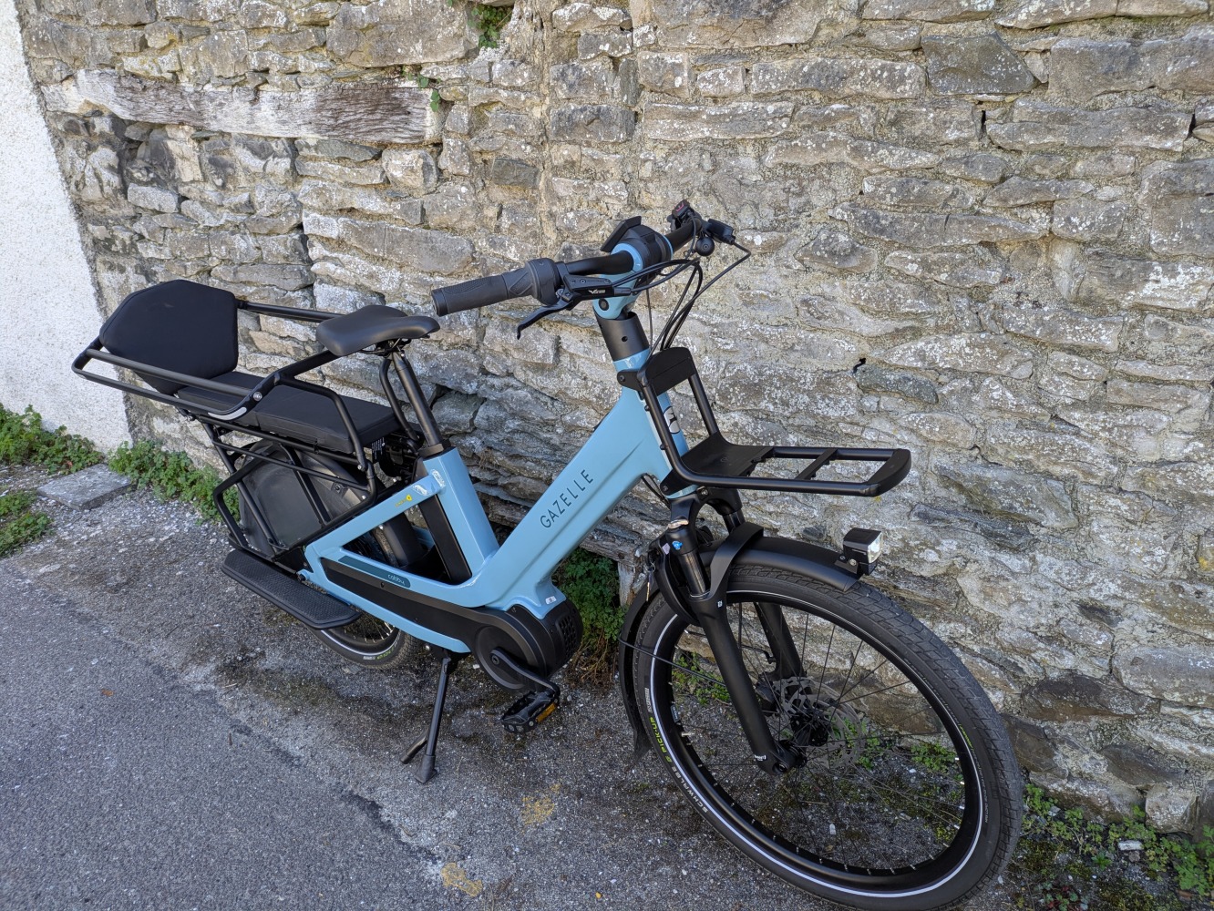 The blue Gazelle Cabby e-cargo bike leant against a wall
