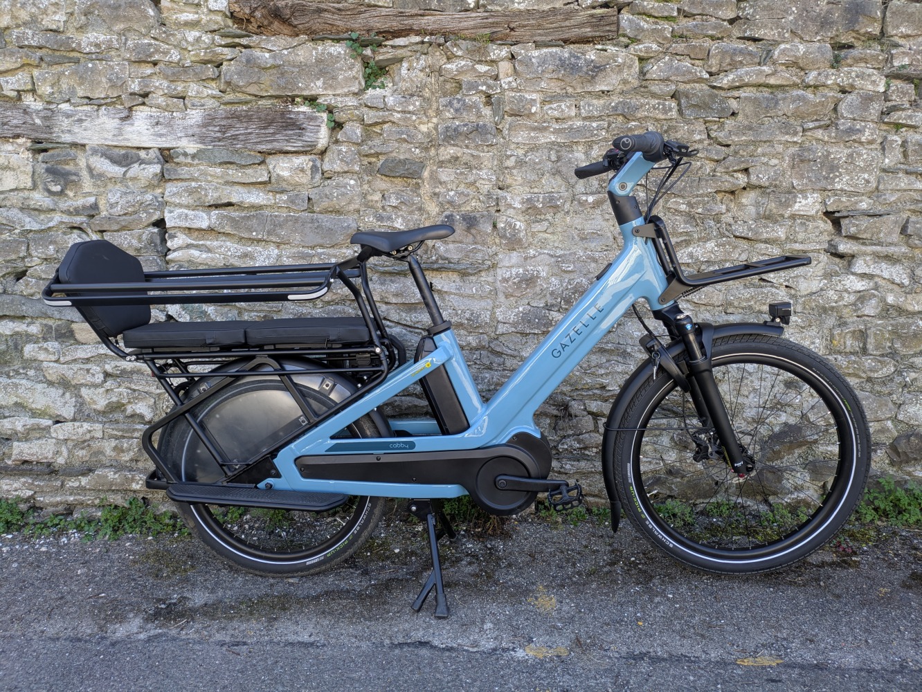 The blue Gazelle Cabby e-cargo bike leant against a wall