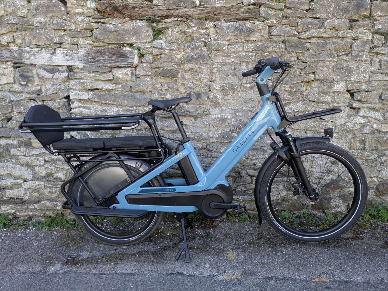 The blue Gazelle Cabby e-cargo bike leant against a wall