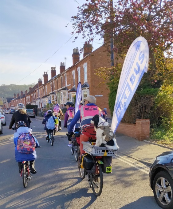 Bike Bus showing a child cycling next to a volunteer carrying a dog on the back of their bike