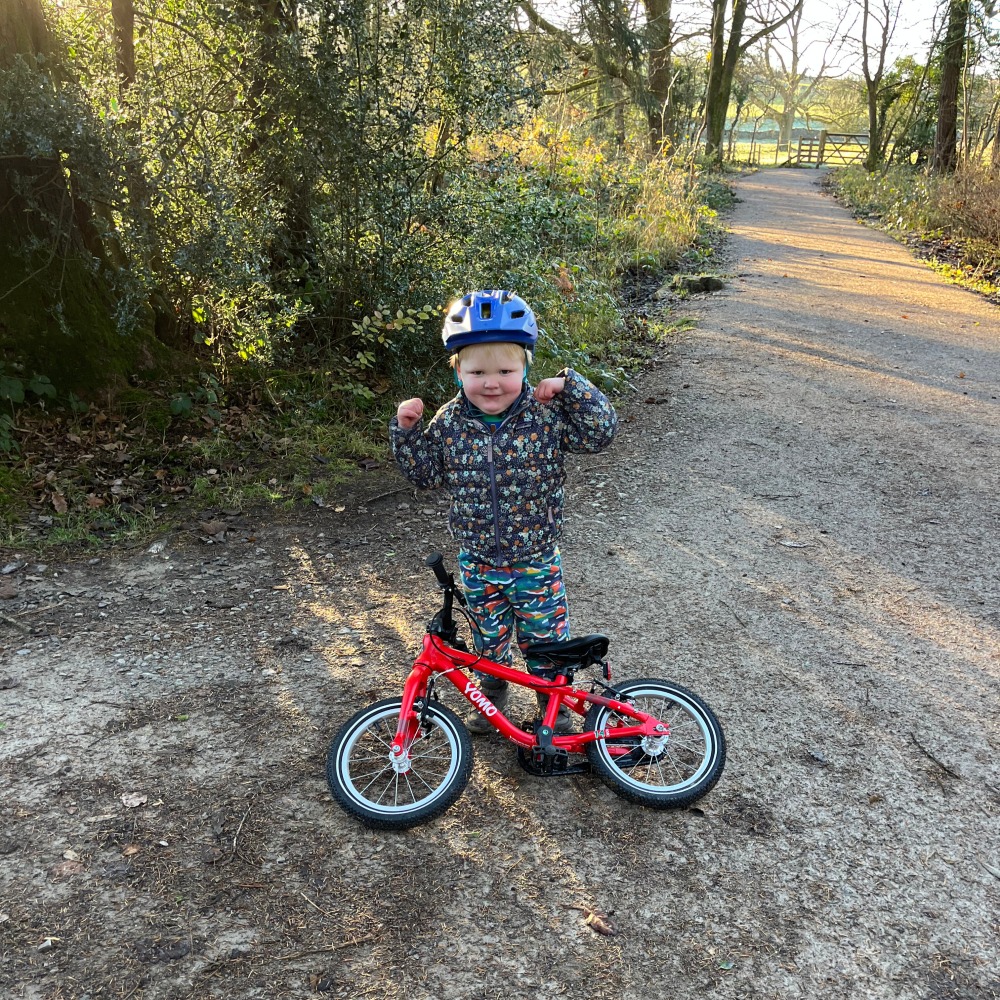 A little boy riding his red yomo bike with a blue helmet on a gravel path on a sunny day