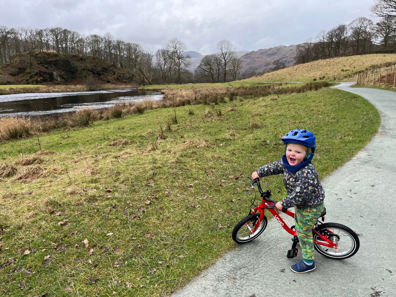 A little boy riding his red yomo bike with a blue helmet on a gravel path on a sunny day