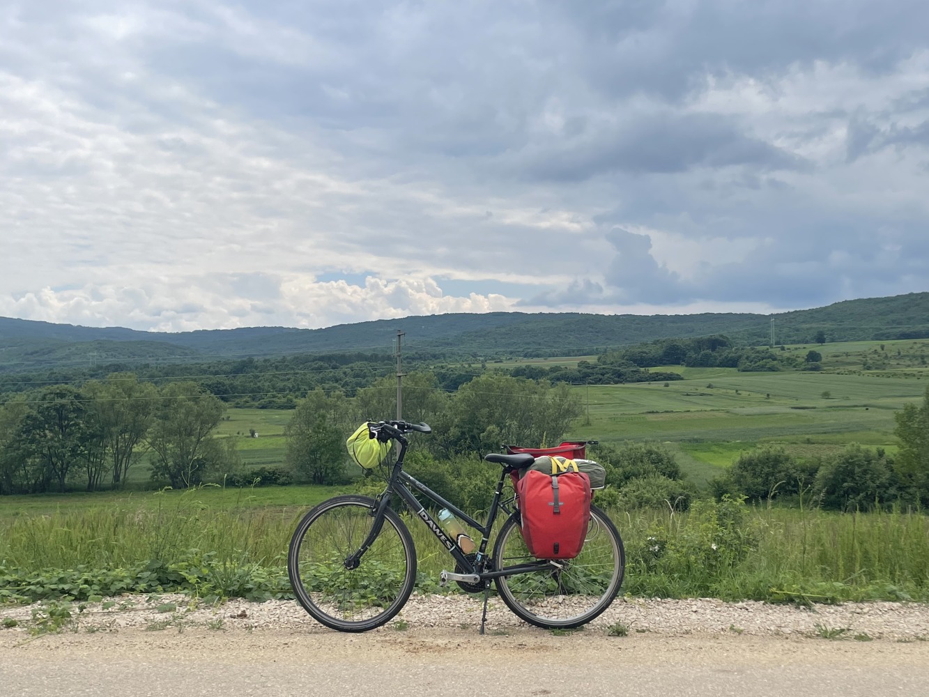 Sahir's touring bike, loaded up with bags, propped up in front of a countryside landscape