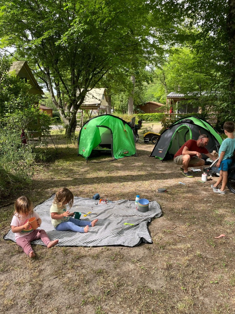 a family campsite with two green tents and two toddlers sat on a picnic rug