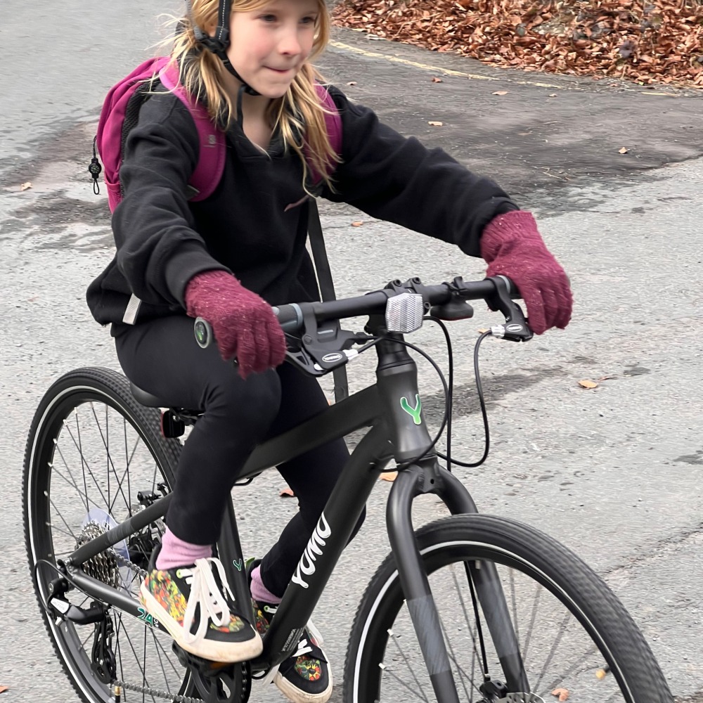 YOMO 24 review- a girl wearing black with a pink backpack and gloves is riding to school