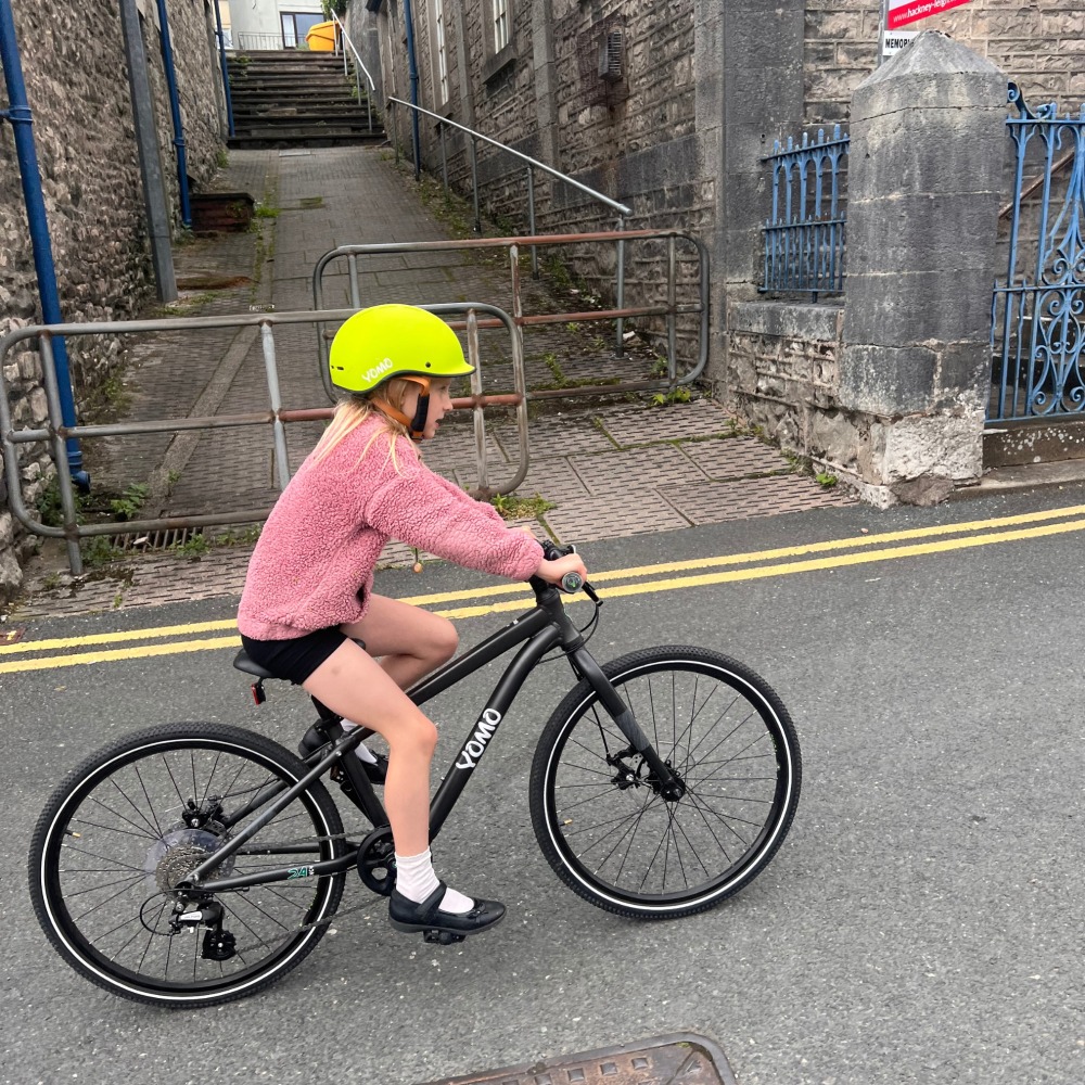 YOMO 24 review- a girl in a pink jumper and yellow helmet is riding along a road