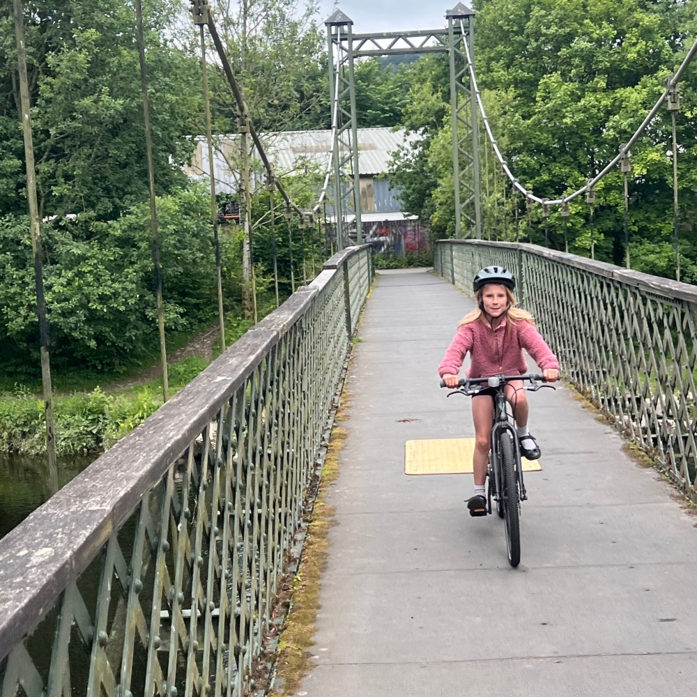 YOMO 24 review- a girl in a pink jumper and yellow helmet is riding over a bridge