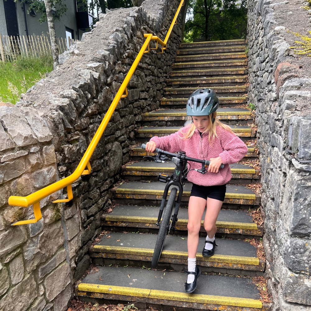 YOMO 24 review- a girl in a pink jumper and yellow helmet is carrying the yomo 24 bike down some stairs