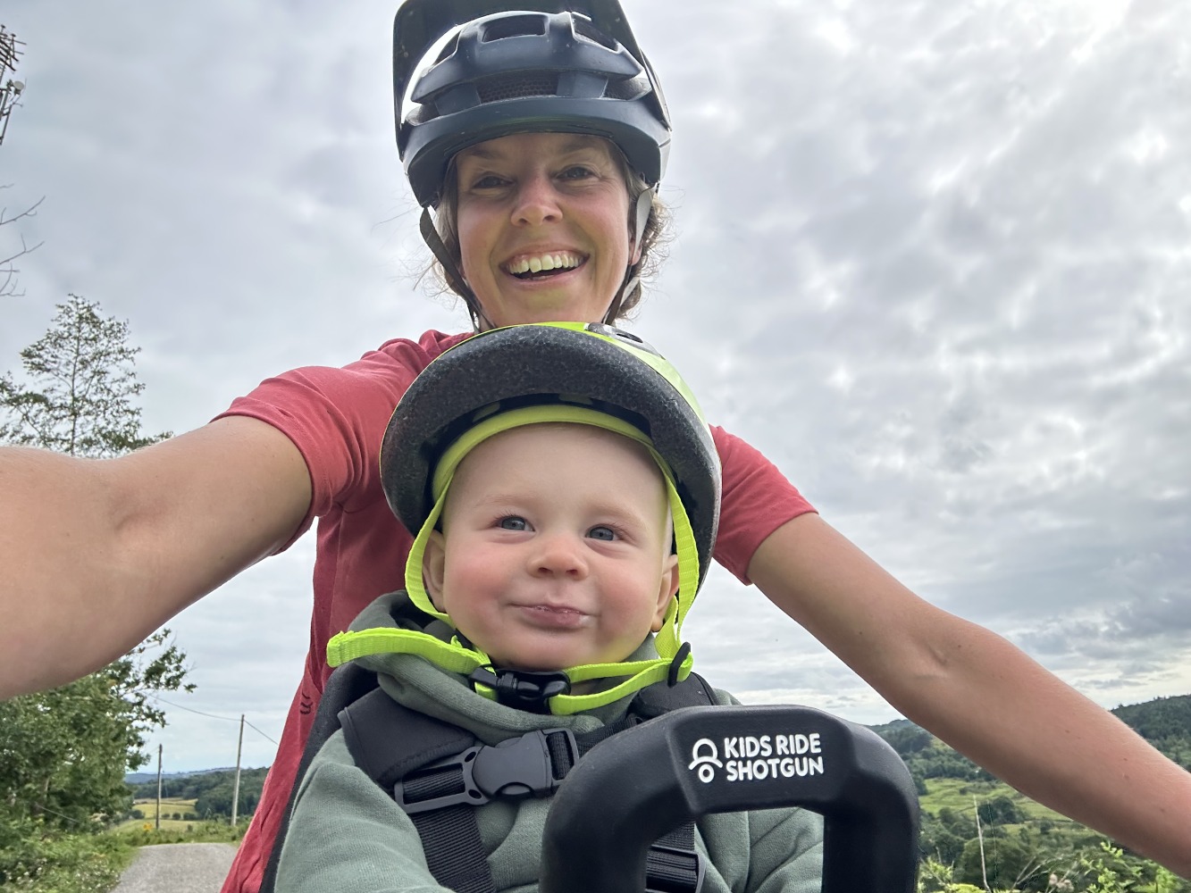 kids ride shotgun pro evo baby seat review- a photos of a little boy in a yellow helmet smiling on a bike ride with his mum