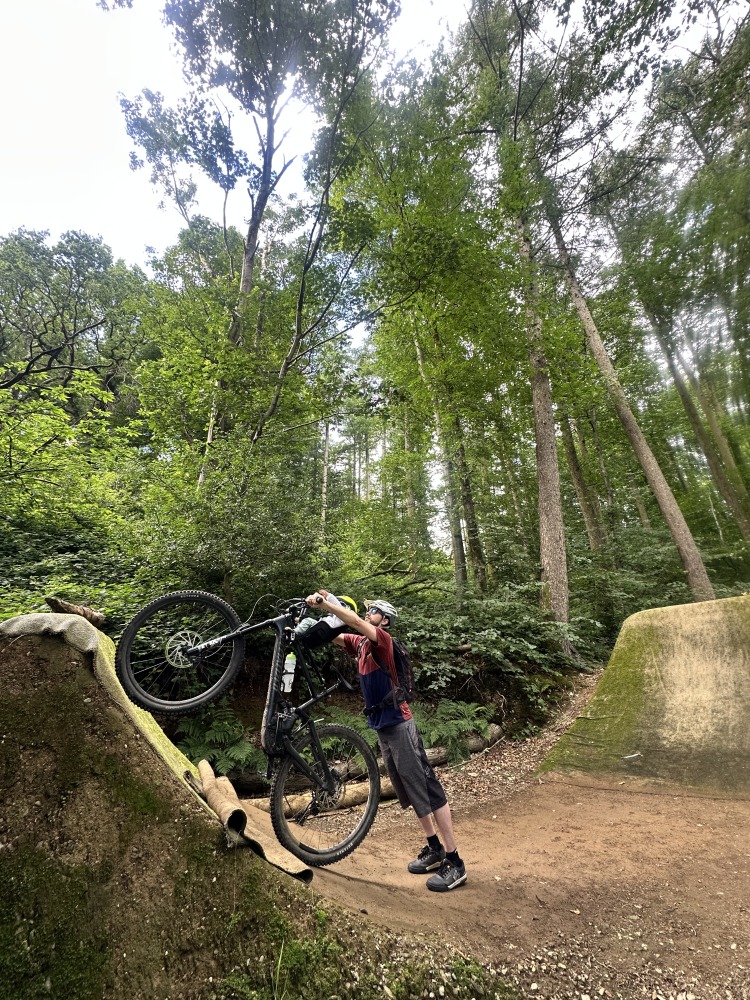 A little boy with a yellow helmet and sunglasses smiling on the kids ride shotgun pro evo eat with his dad pretending to ride a massive jump