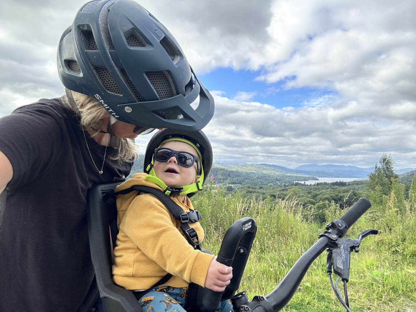 kids ride shotgun pro evo baby seat review- a photos of a little boy in a yellow helmet smiling on a bike ride with his mum