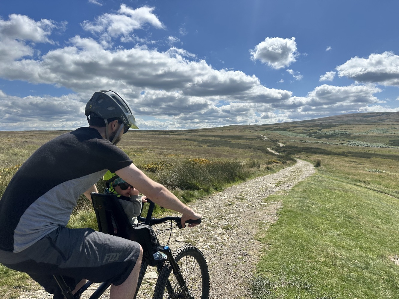 A little boy with a yellow helmet and sunglasses smiling on the kids ride shotgun pro evo eat with his dad