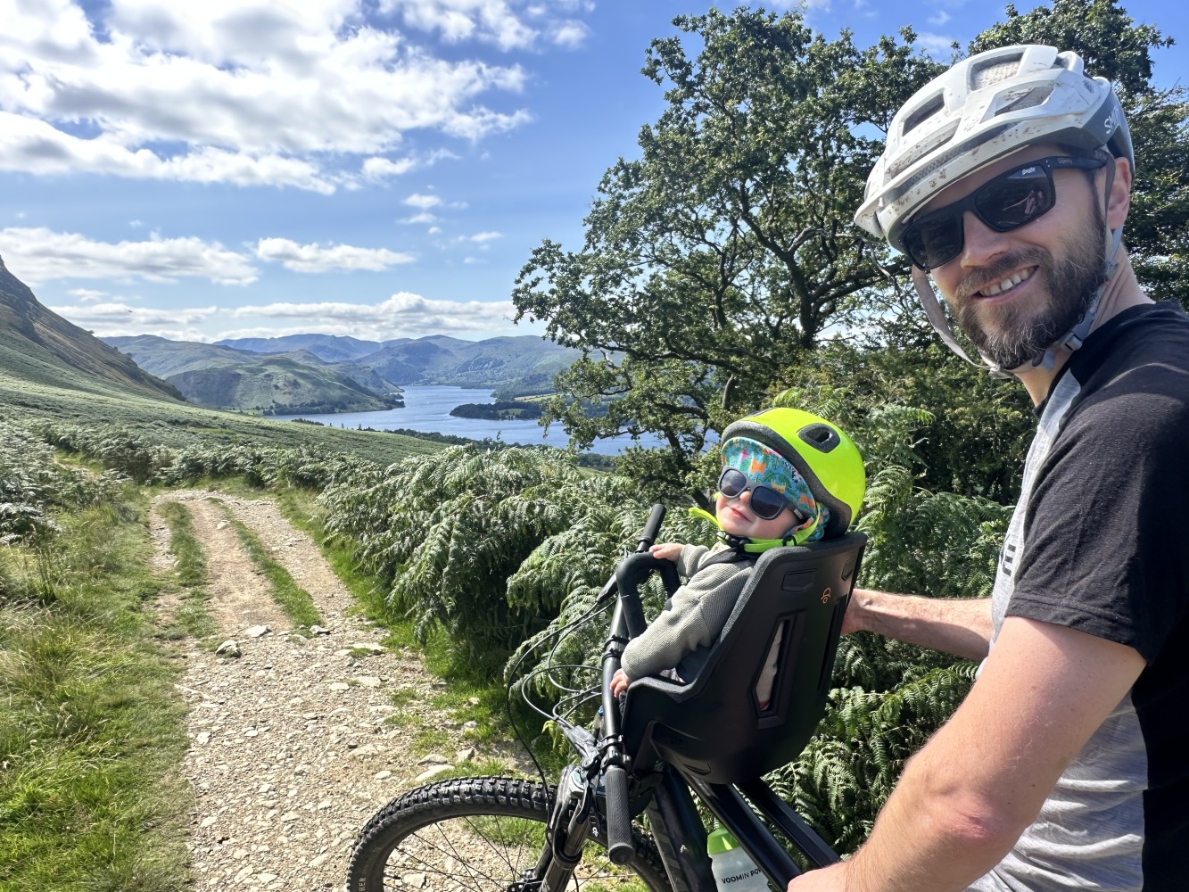 A little boy with a yellow helmet and sunglasses smiling on the kids ride shotgun pro evo seat with his dad