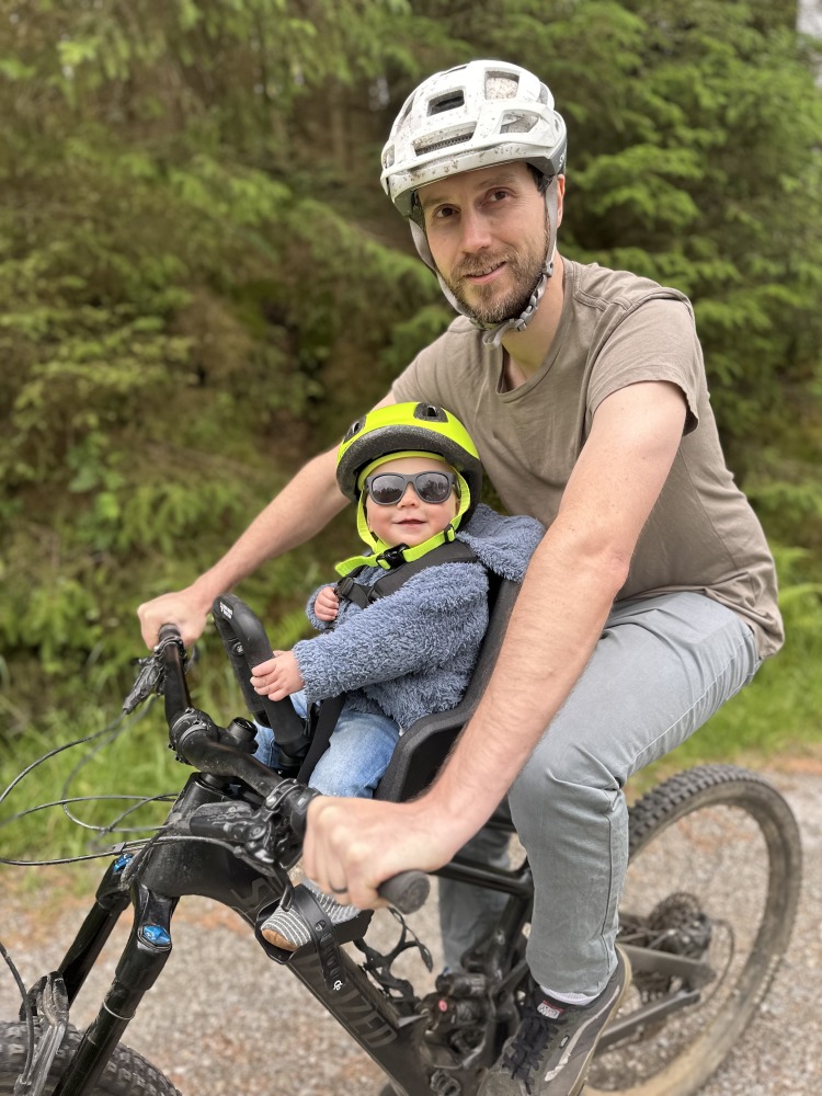 A little boy with a yellow helmet and sunglasses smiling on the kids ride shotgun pro evo eat with his dad