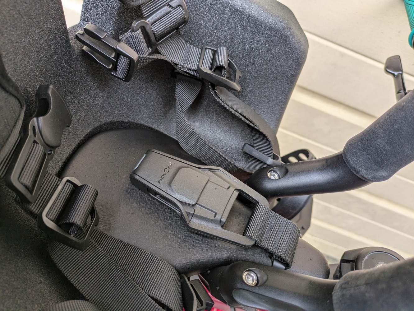 A Kids Ride Shotgun Pro Evo reat mounted to a red mountain bike leant against a garage door- a close up of the fidlock buckle