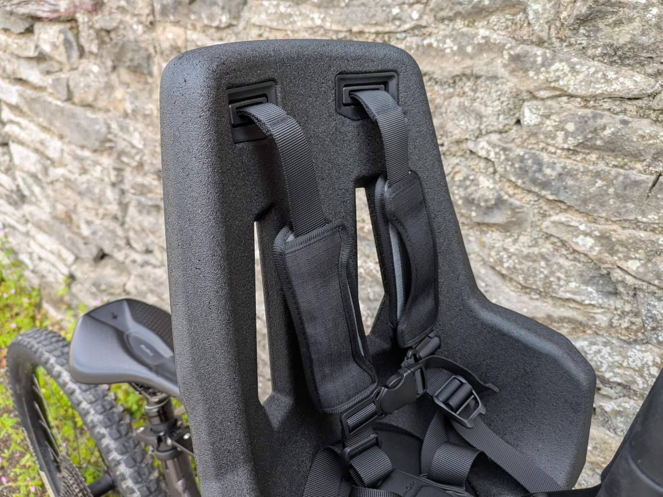 A Kids Ride Shotgun Pro Evo reat mounted to a red mountain bike leant against a stone wall- a close up of the straps