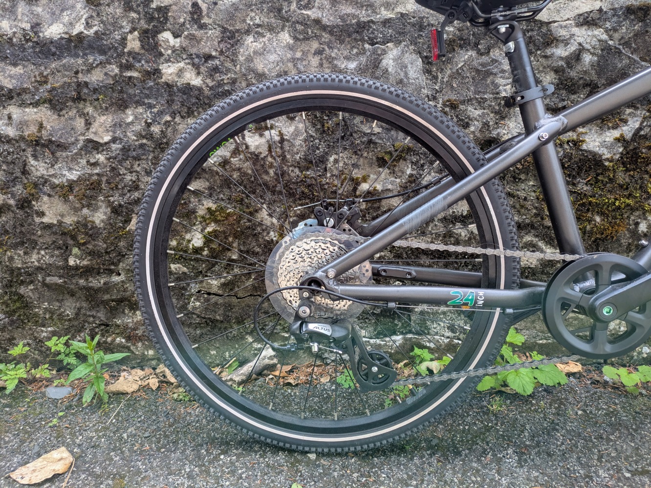 YOMO 24 review- the grey bike leant against a stone wall, close up of the rear wheel and gears