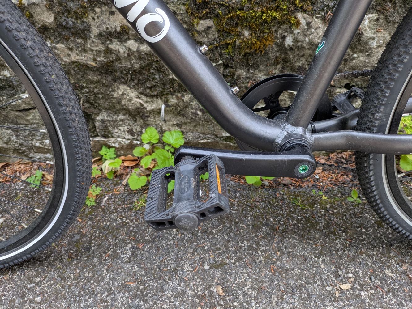 YOMO 24 review- the grey bike leant against a stone wall, close up of the pedal