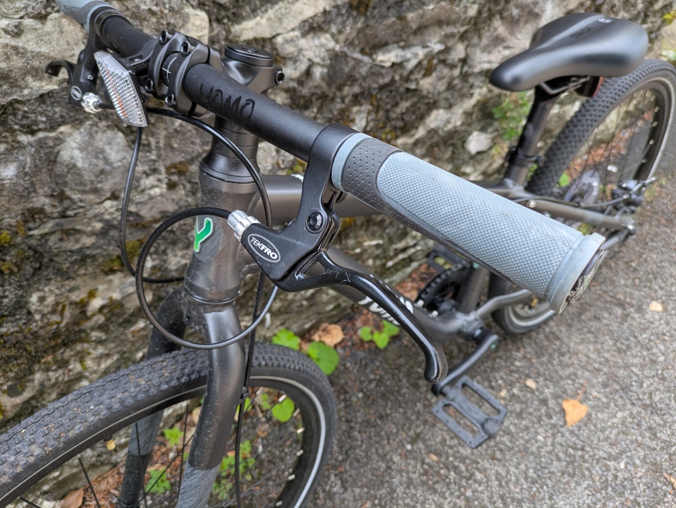 YOMO 24 review- the grey bike leant against a stone wall, close up of the brake leaver