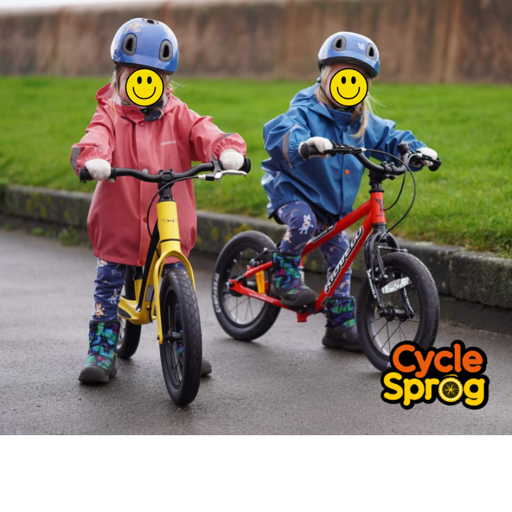 Photo of twin 3 year old girls. One is riding a yellow balance bike and the other a red pedal bike