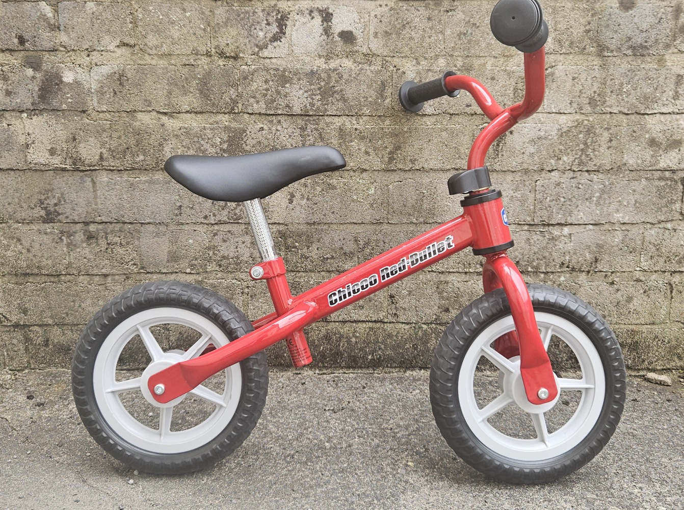 Red Chicco balance bike up against a brick wall