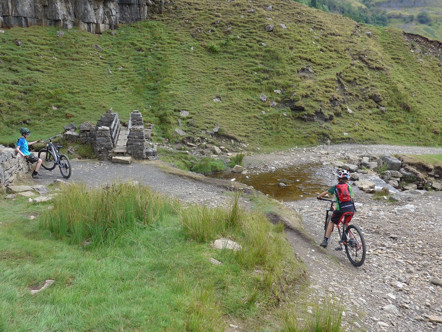 A couple of boys on their mountain bikes traversing a rocky track leading to a small bridge