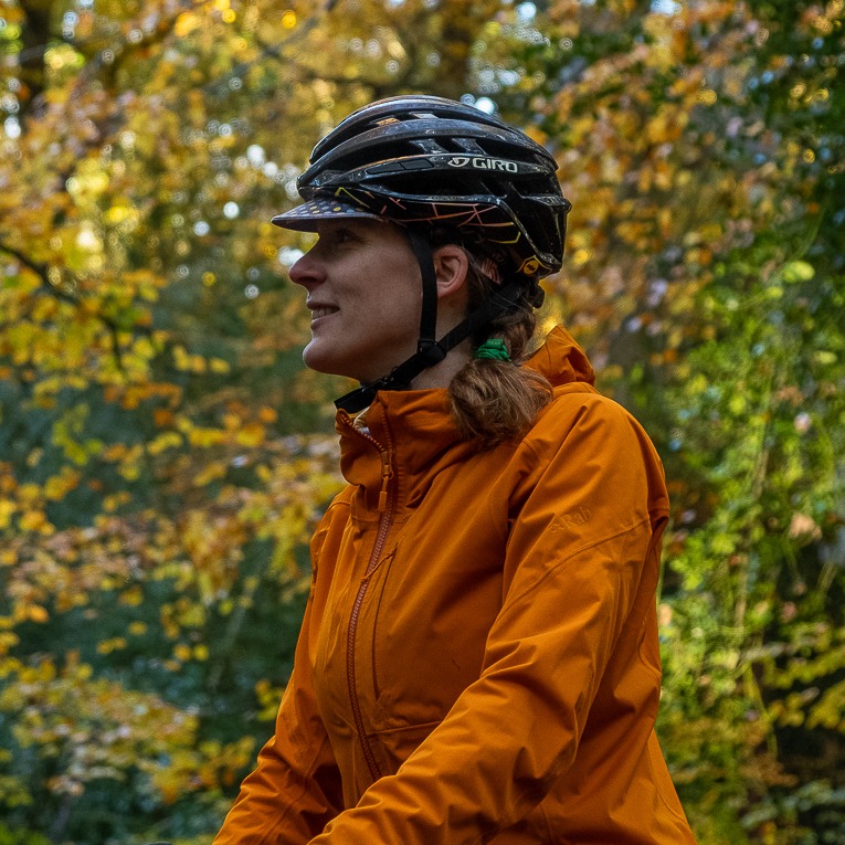 Hetty Kingston seen from the side, wearing a waterproof jacket and bike helmet, with trees behind her