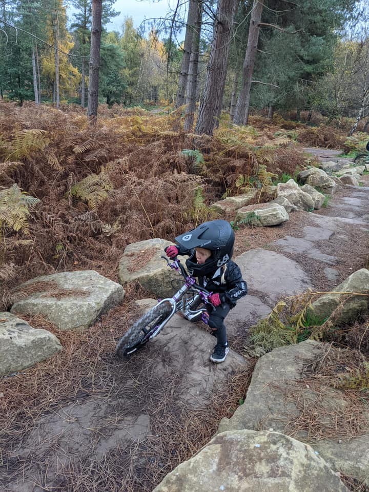 A little girl in a full face helmet wheeling her mountain bike over some large rocks