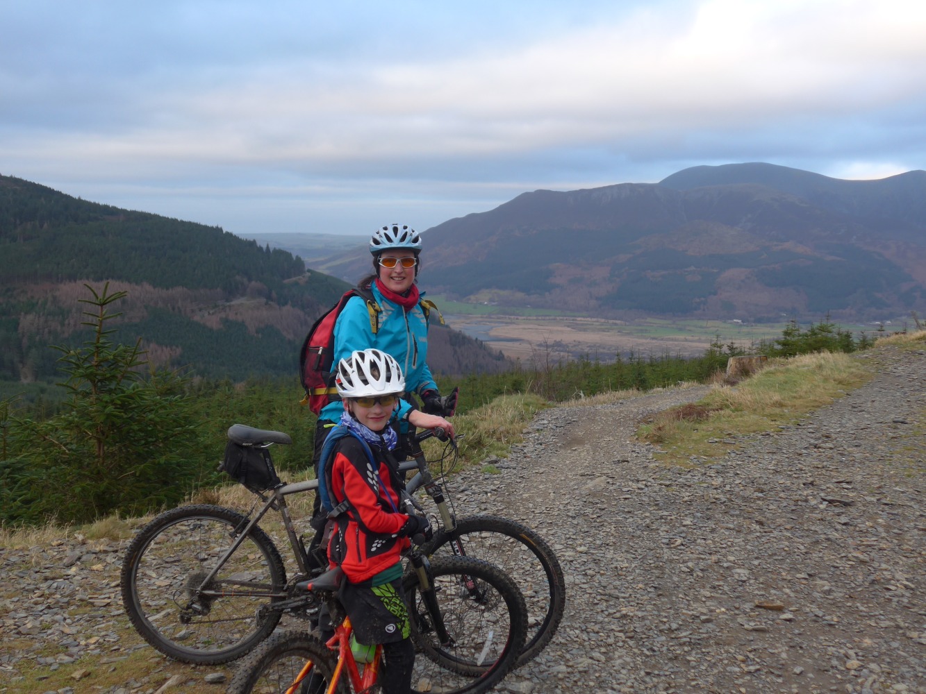 A woman and her son standing with their bikes on a rocky path with the Cumbrian mountains in the background