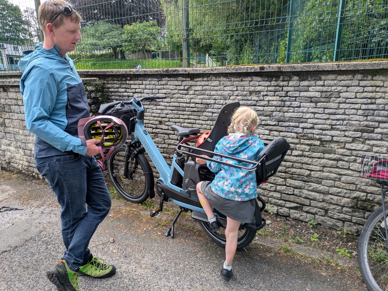 Gazelle Cabby review- a dad in a blue coat and orange with his daughter in a blue jacket and pink helmet and school dress climbing about at the school gate