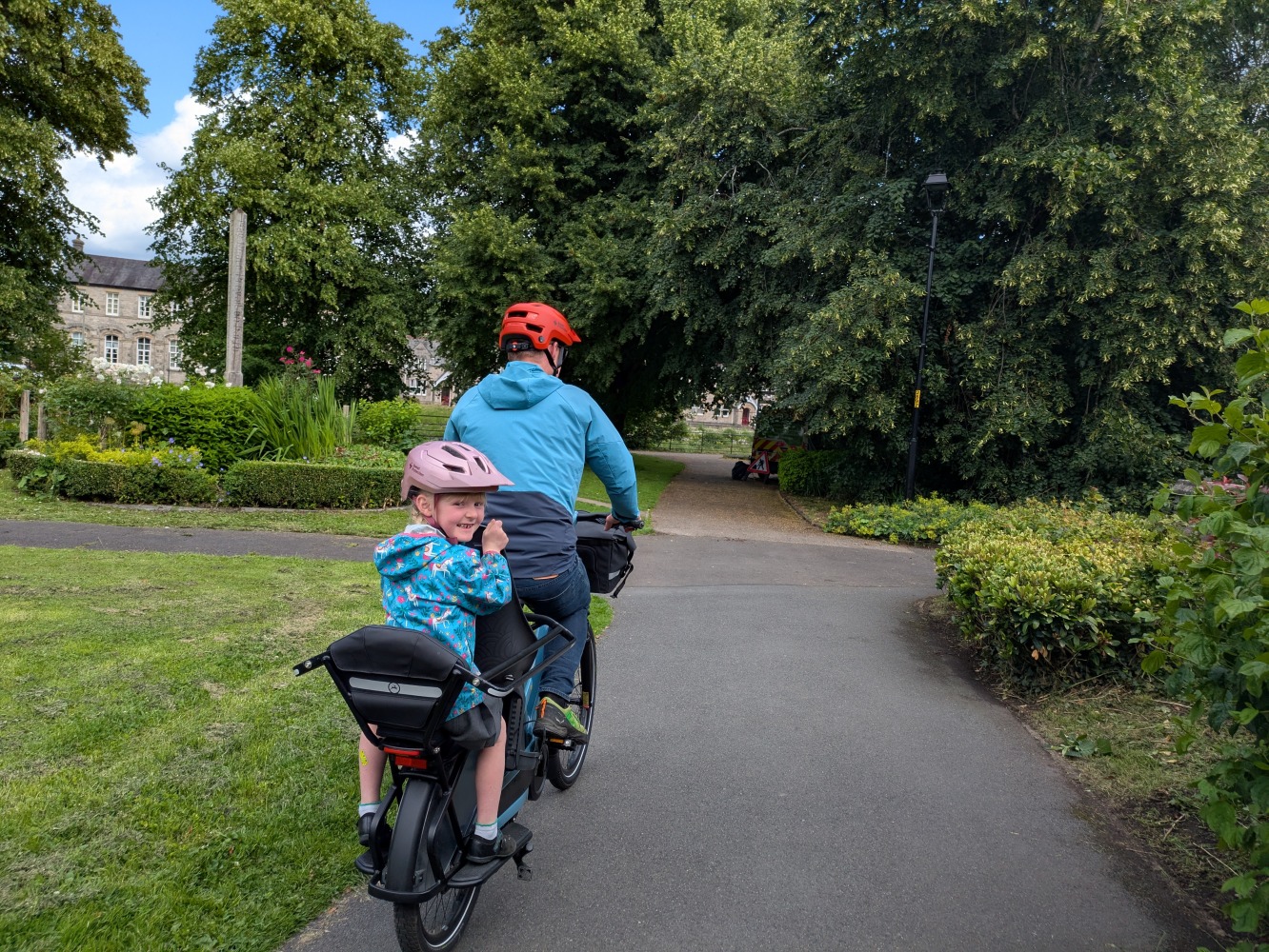 Gazelle Cabby review- a dad in a blue coat and orange with his daughter in a blue jacket and pink helmet and school dress riding the gazelle cabby in the park