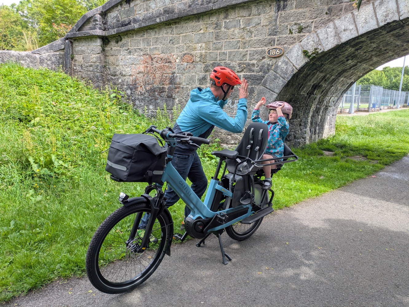 Gazelle Cabby review- a dad in a blue coat and orange helmet riding the gazelle cabby with his daughter in a blue jacket and pink helmet and school dress, they are high fiving