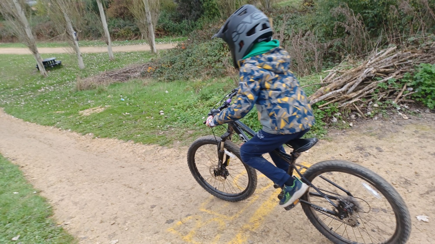 A child on a mountain bike with a full face helmet, riding down a dirt track, seen from behind
